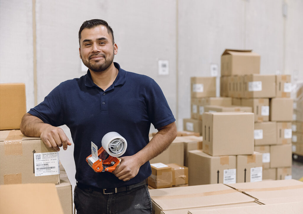 Worker Holding a Labelling Machine Surrounded by Boxes in Warehouse