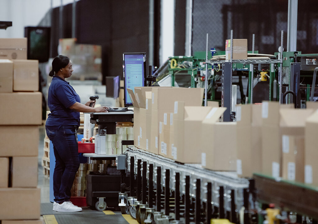 Certified Female Staff in Warehouse Performing Checks with Line of Supply Boxes