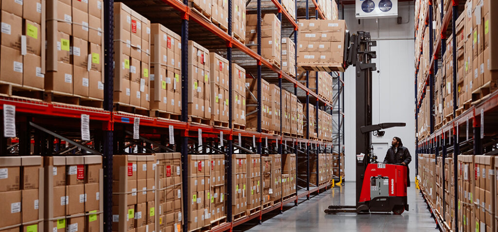 Worker in Warehouse Surrounded by Tall Walls of Boxes Providing SSaaS for Clients